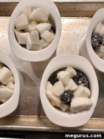 Blackberry apple filling generously spooned into individual ramekins, ready for the crumble topping.