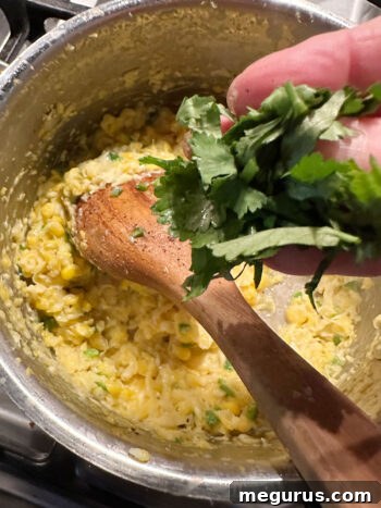 adding cilantro to corn in saucepan to finish the creamed corn