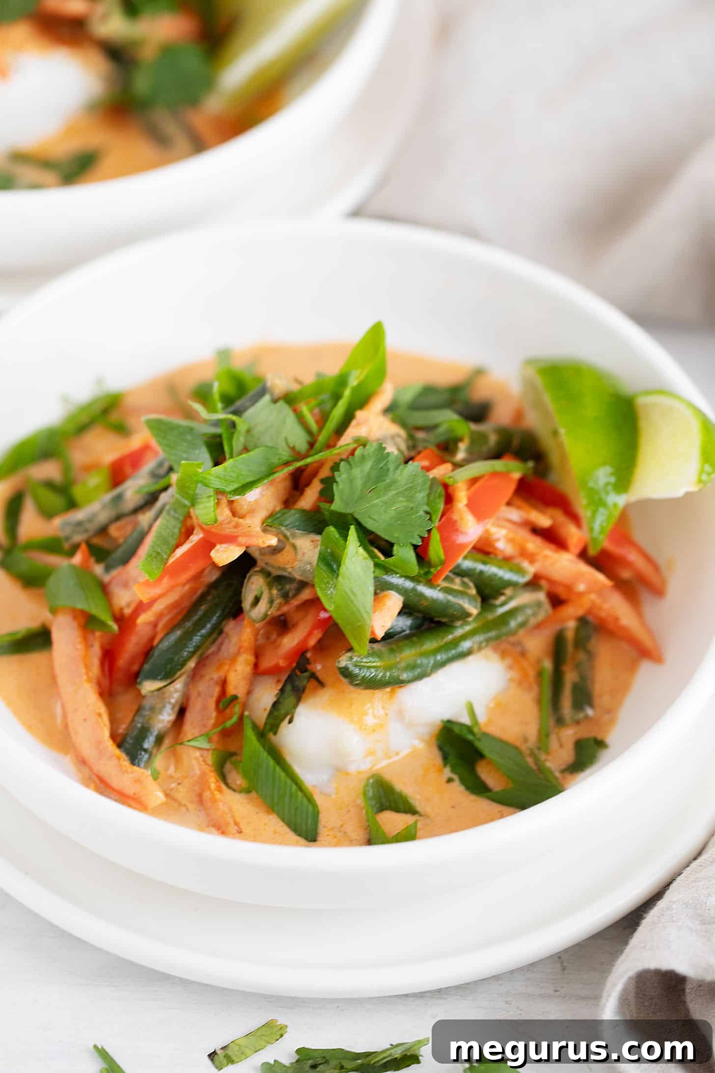 Two bowls of Thai red curry fish garnished with cilantro and lime