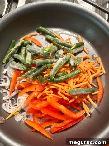 Sautéing shallots, bell pepper, carrots, and green beans in a skillet