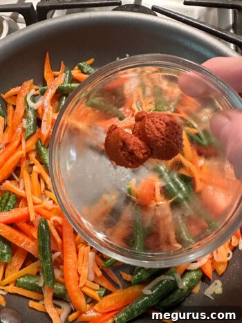 Adding Thai red curry paste to the sautéed vegetables in the skillet