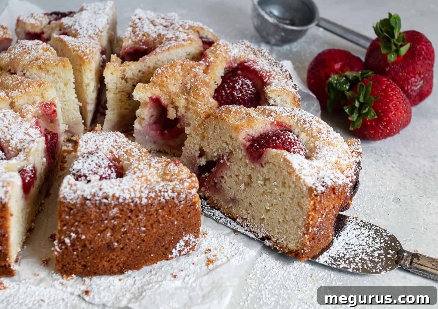 Sliced rustic strawberry cake revealing a generous amount of fruit, resting on parchment paper.