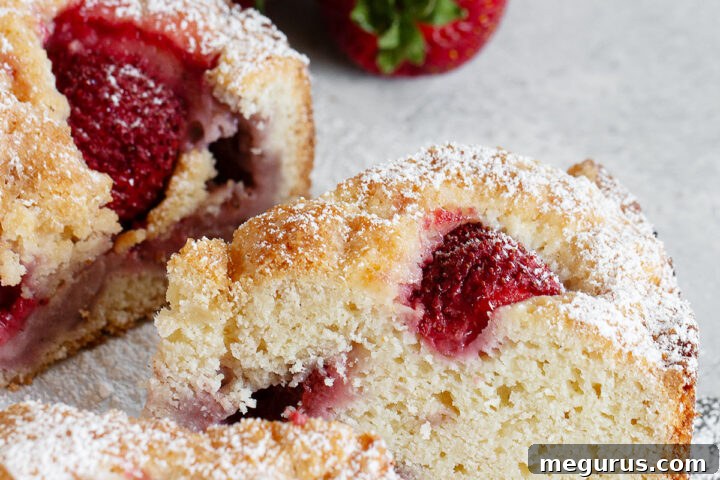 A slice of rustic strawberry cake on a wooden board, showcasing the moist interior and abundance of strawberries.