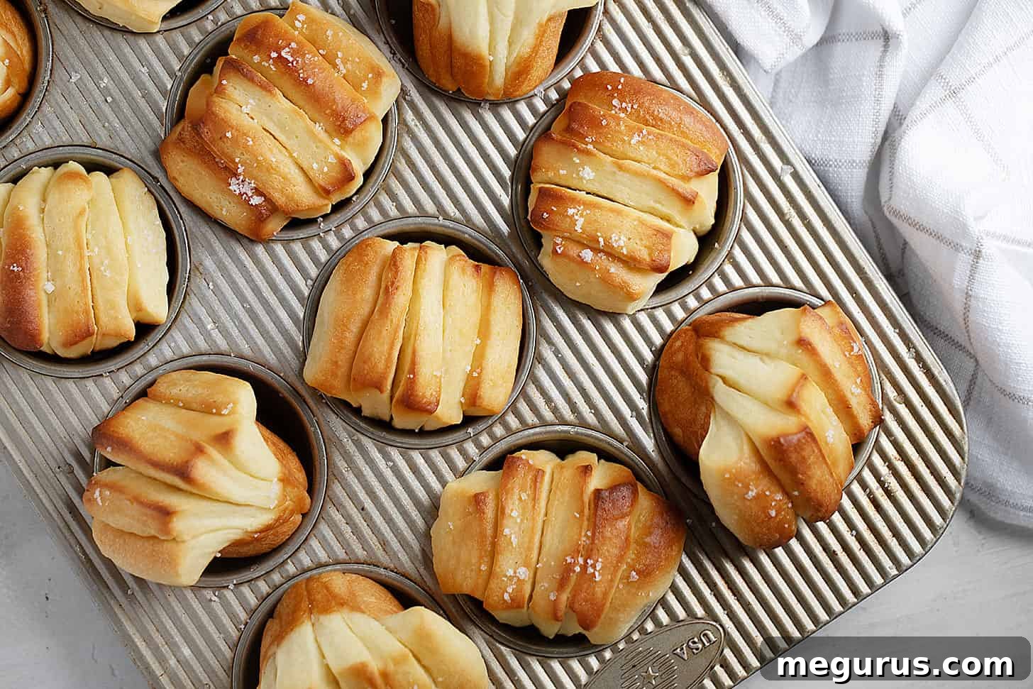 Golden brown Butterflake rolls, freshly baked and arranged in a muffin tin, ready to be served.