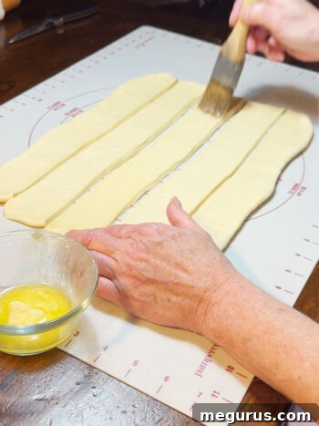 Brushing melted butter onto a dough strip before stacking.