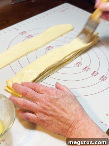 A close-up of a stacked dough strip being brushed with butter.