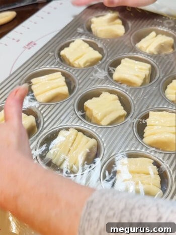 Muffin tin with rolls covered in plastic wrap for the second rise.