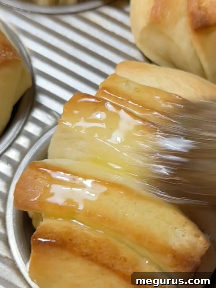 Freshly baked butterflake rolls being brushed with melted butter after coming out of the oven.