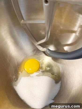 Egg and sugar being creamed together in a stand mixer with a paddle attachment.