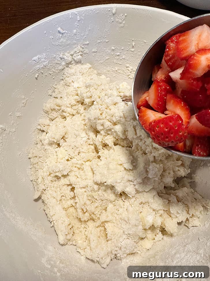 Diced fresh strawberries being added to the muffin batter in a mixing bowl