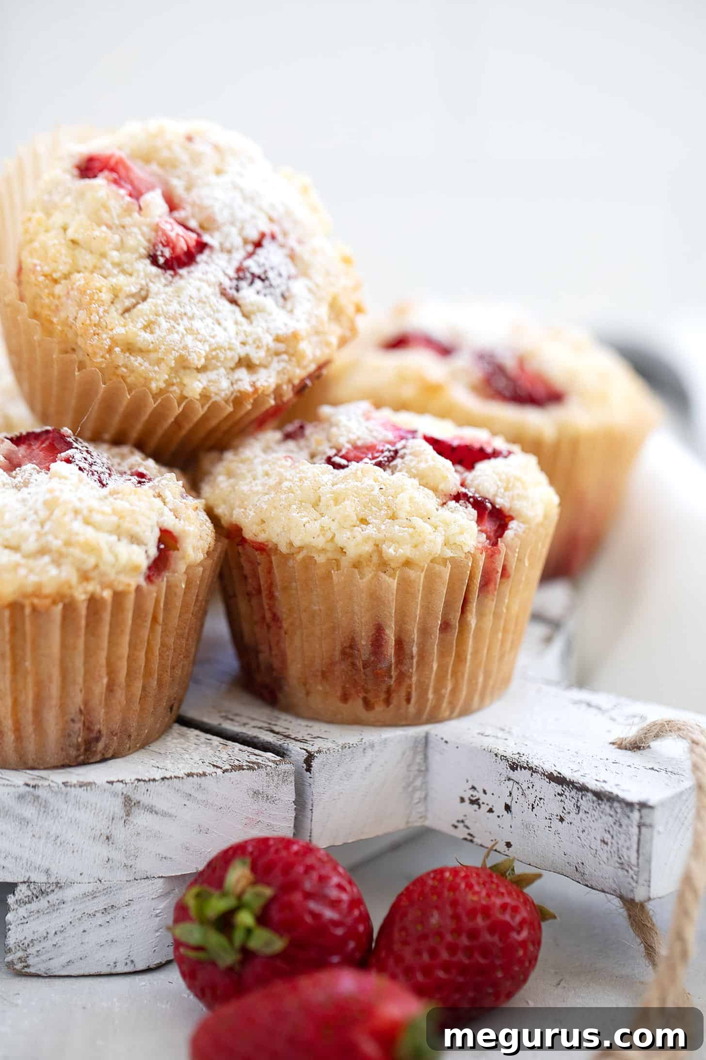 Close-up of baked strawberry shortcake muffins on a serving board, dusted with powdered sugar
