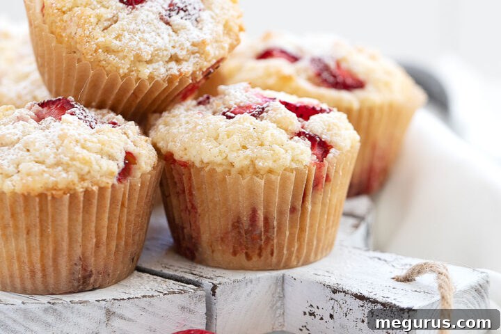 A close-up shot of a single strawberry shortcake muffin on a white plate, showcasing its tender crumb and baked-in strawberries