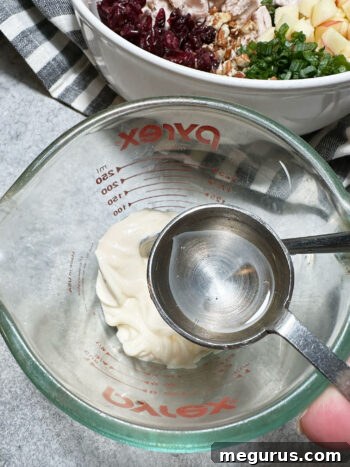Adding white vinegar to mayonnaise in a clear measuring cup for the dressing.