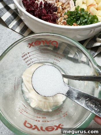 Adding granulated sugar to the dressing mixture in a measuring cup.