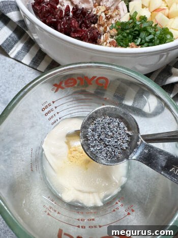 Adding poppy seeds to the mixed dressing in a measuring cup before stirring.