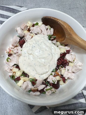 Pouring the creamy dressing over the mixed turkey salad ingredients in a large bowl.