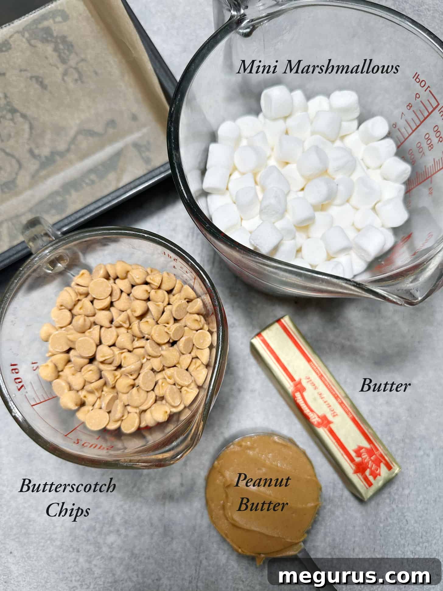 A selection of ingredients laid out on a table: mini marshmallows, butterscotch chips, peanut butter, and butter, ready for making dessert.