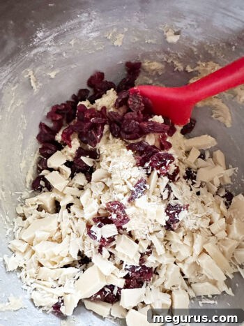 White chocolate chips being added to the cookie dough for even distribution.