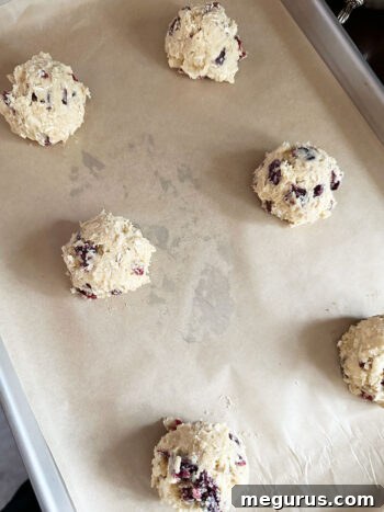 Portioned cookie dough scoops evenly spaced on a parchment-lined baking sheet, prepared for the oven.