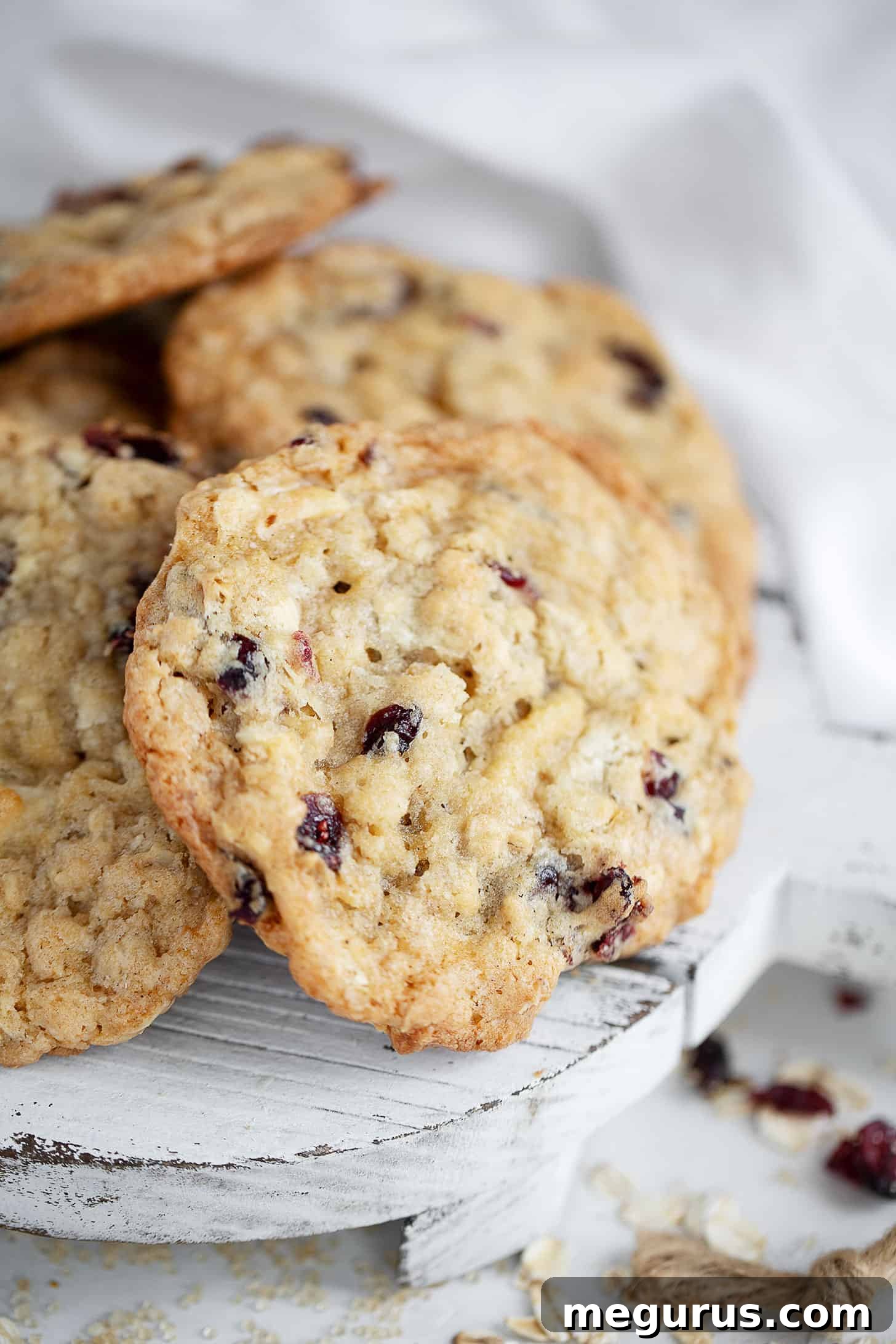 A close-up shot of freshly baked cranberry oatmeal white chocolate cookies on a wooden board, highlighting their golden edges and chewy texture.