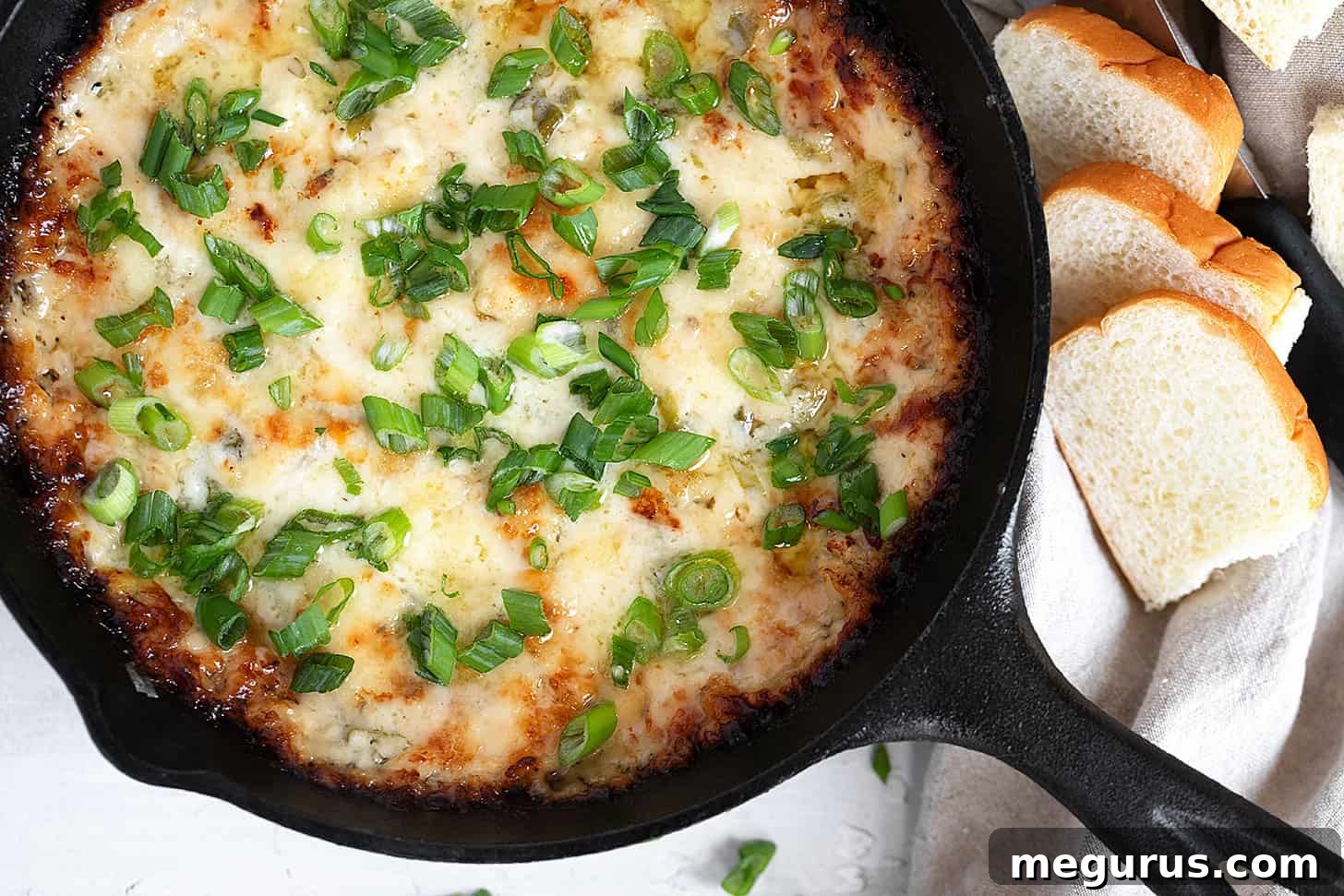 Warm, golden-brown hot onion and cheese dip in a rustic cast iron skillet, surrounded by toasted bread slices ready for dipping. This French onion soup inspired appetizer is perfect for parties.