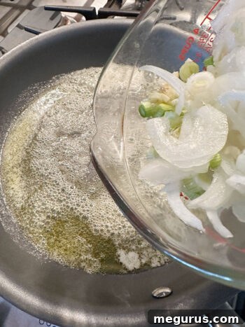 Sliced onions and garlic being added to a hot skillet with melted butter and oil, ready to start cooking.