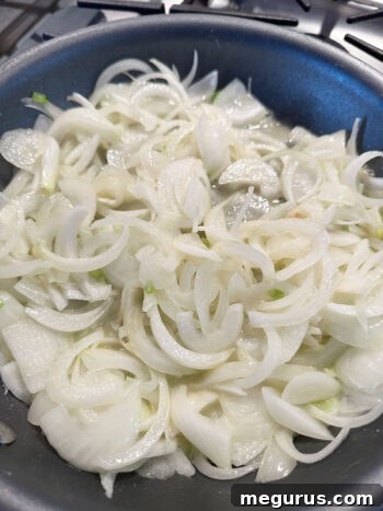 Onions cooking gently in a skillet, gradually softening and beginning to take on a translucent appearance.