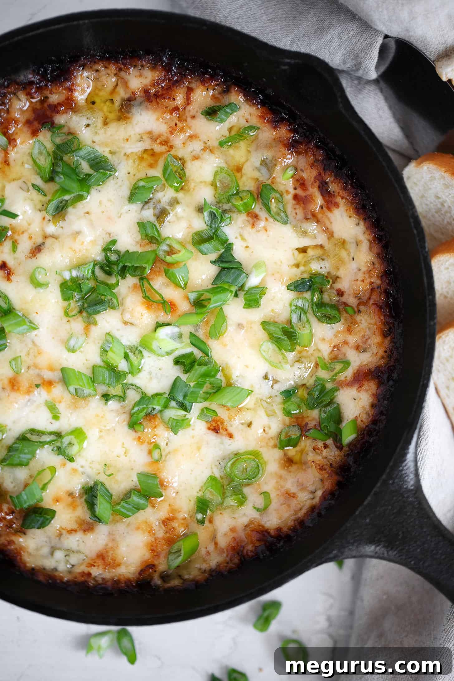 Close-up of a bubbling hot onion dip in a cast iron skillet, garnished with fresh green onions, ready to be served as an appetizer.