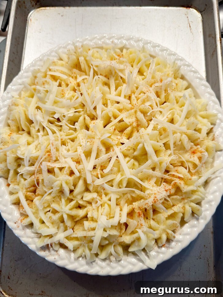 Assembled fish pie with piped mashed potato topping, shredded cheese, and paprika, ready for baking