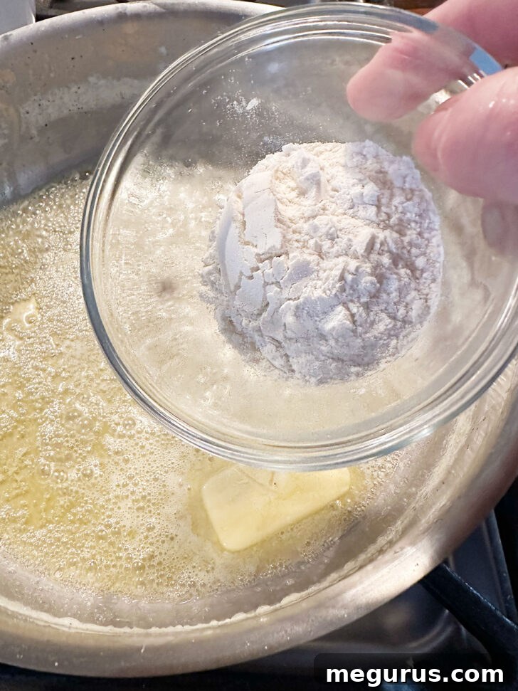 Adding flour to melted butter in a skillet to make a roux