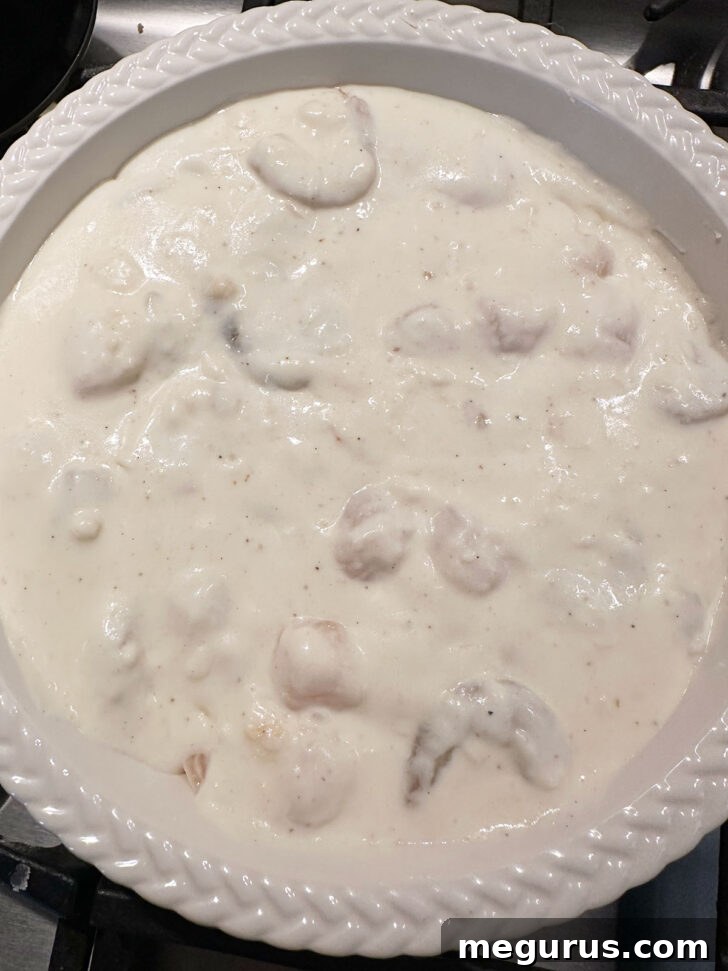 Pouring the creamy seafood sauce over the poached fish in a baking dish