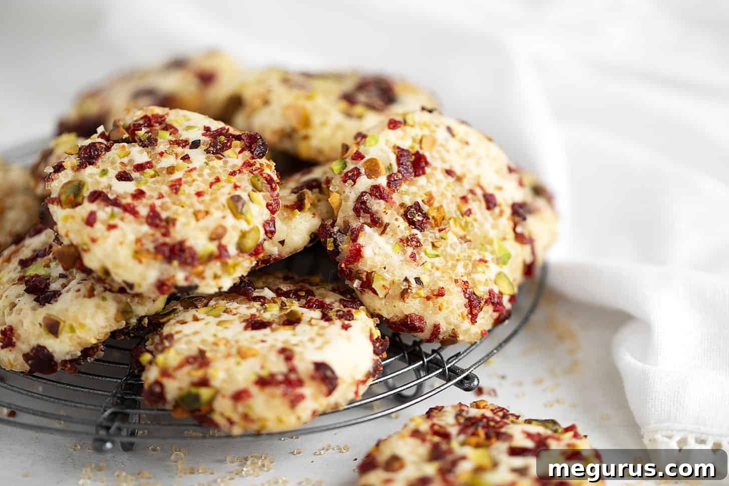 Delicate shortbread cookies adorned with festive pistachios and cranberries, cooling on a wire rack.