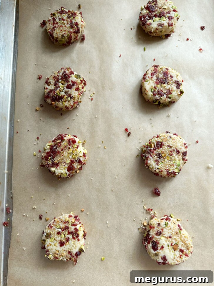 Flattened pistachio cranberry cookies on a baking sheet, ready for final chilling and baking.