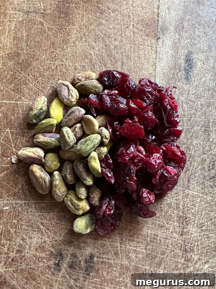 Raw pistachios and dried cranberries on a cutting board, ready for chopping.