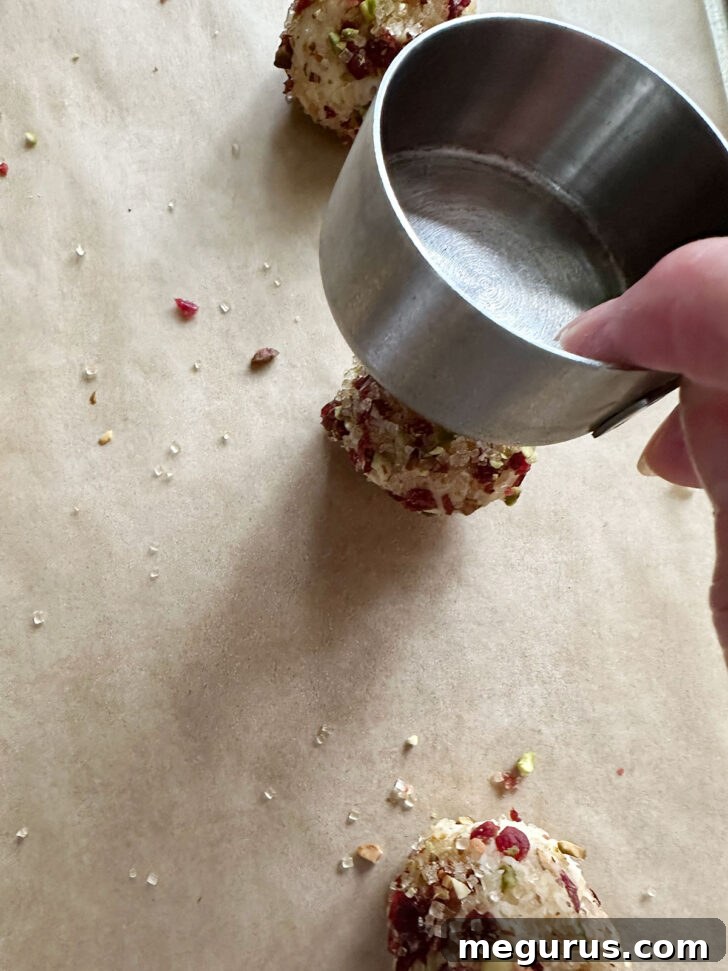 Flattening cookie dough balls with the bottom of a measuring cup to create uniform discs.