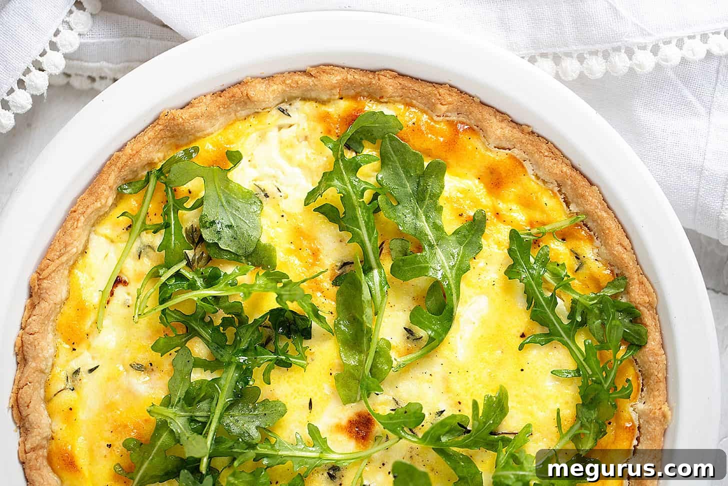Rustic goat cheese quiche in a ceramic baking dish, garnished with fresh arugula and ready to serve.