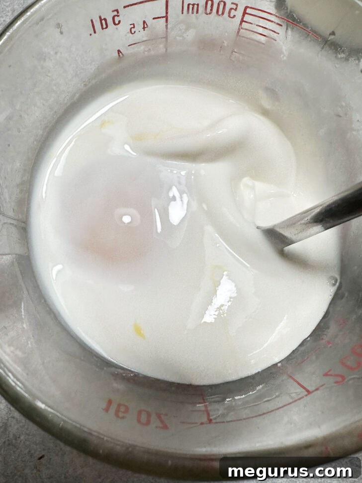 Mixing eggs and cream together in a clear glass measuring cup, forming the base of the quiche custard.