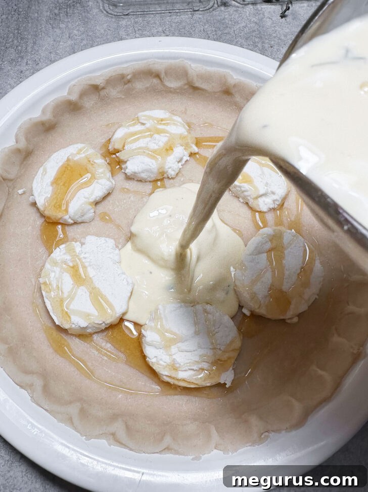 Carefully pouring the prepared egg and cream custard mixture over the honey-drizzled goat cheese in the pie shell.