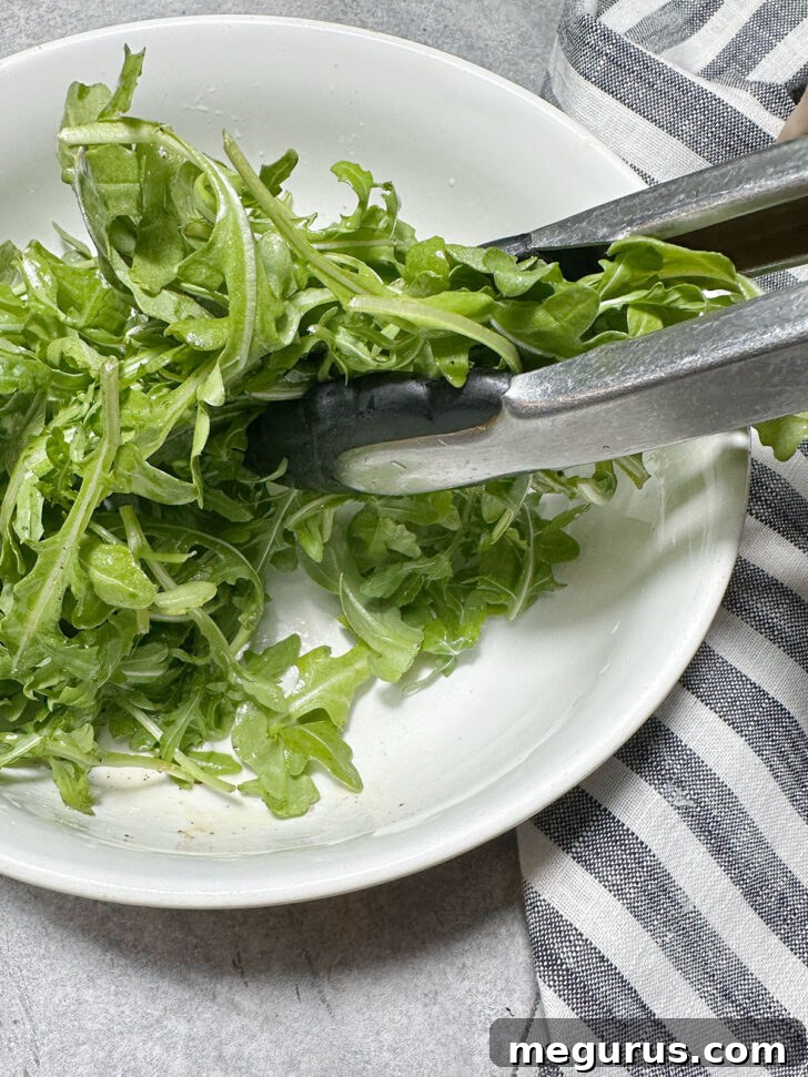 Tossing fresh arugula with olive oil, salt, and pepper in a bowl to prepare the topping for the quiche.