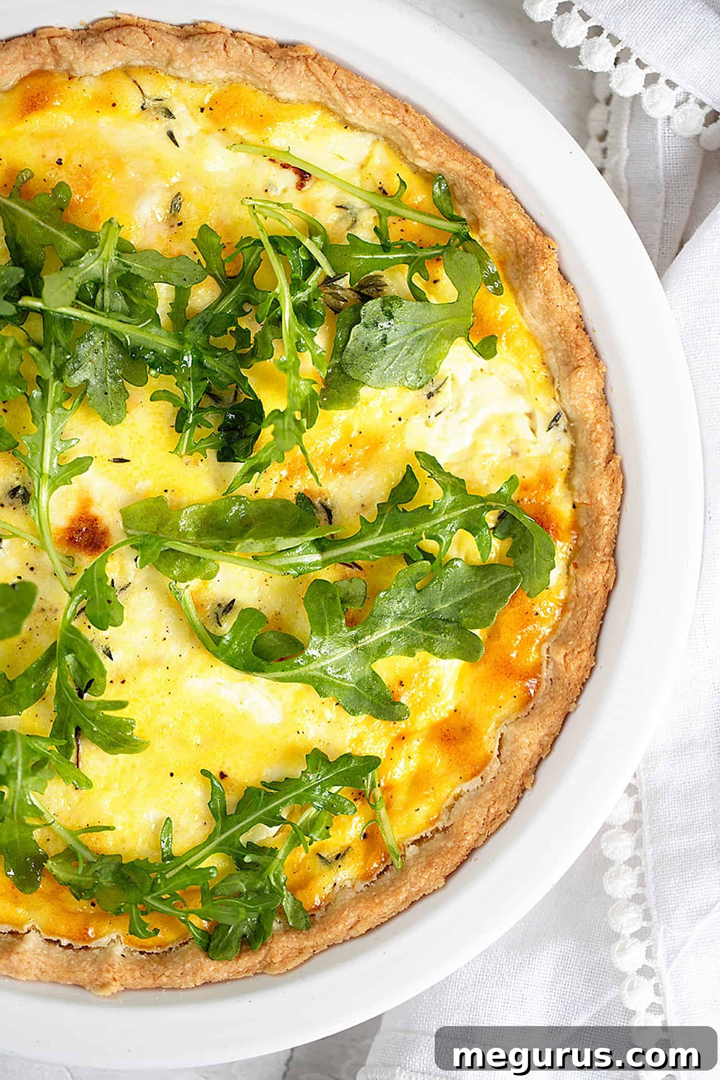 Close-up of the golden-brown goat cheese quiche, still in its baking dish, garnished with a generous serving of fresh arugula.