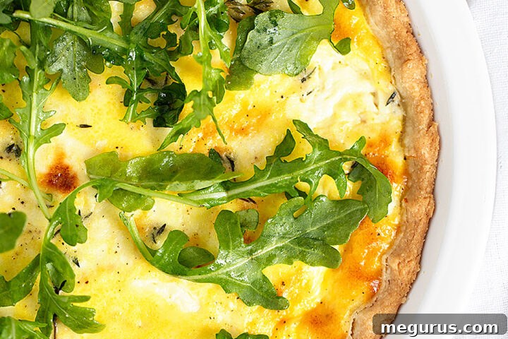 Goat cheese quiche in a baking dish, garnished with fresh arugula on top.