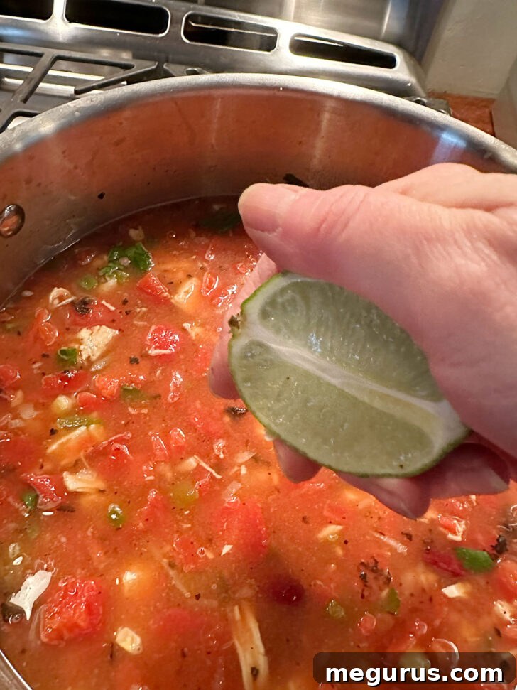 Squeezing fresh lime juice into the finished Mexican chicken soup for a bright, zesty finish.