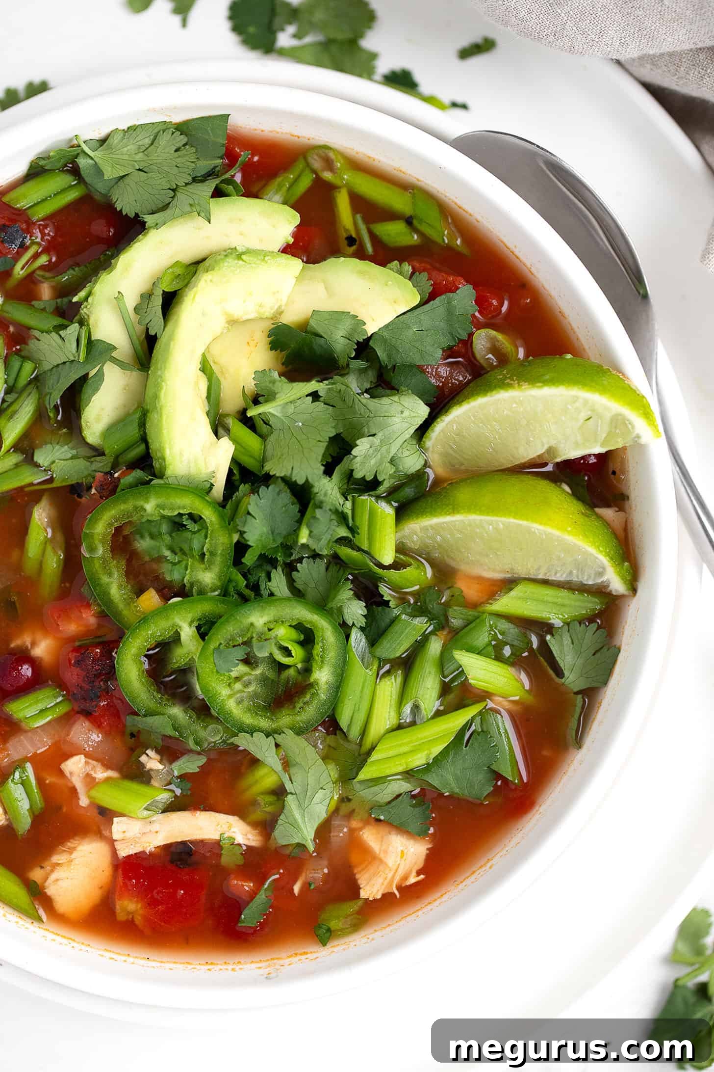 Garnished Mexican chicken soup in a bowl with fresh lime and avocado slices