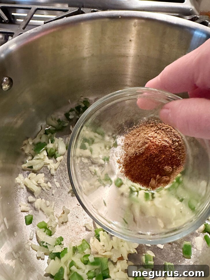 Adding aromatic spices like cumin, coriander, and chili powder to sautéed onions and jalapeños in a large pot for the soup base.
