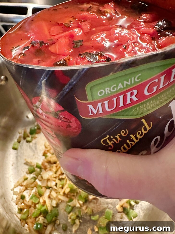 Adding a large can of diced tomatoes, including their juices, to the simmering soup base.