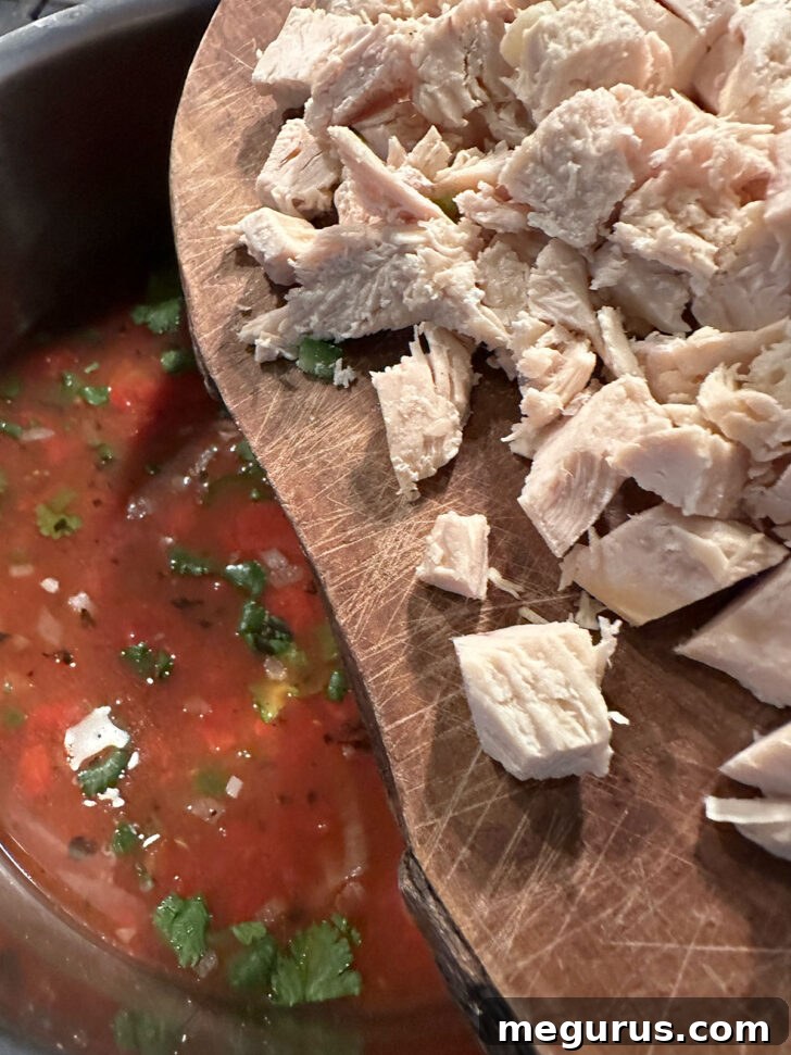 Adding shredded cooked chicken to the soup pot, completing the hearty base.