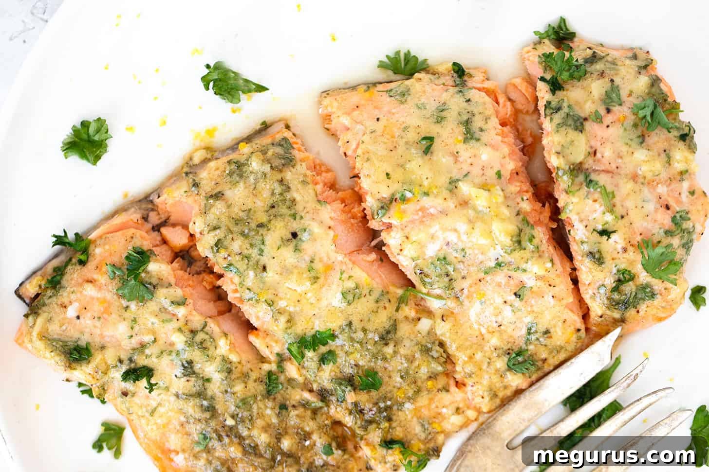 A perfectly cooked dijon garlic salmon fillet rests on a crisp white plate, garnished with fresh herbs and a lemon wedge.