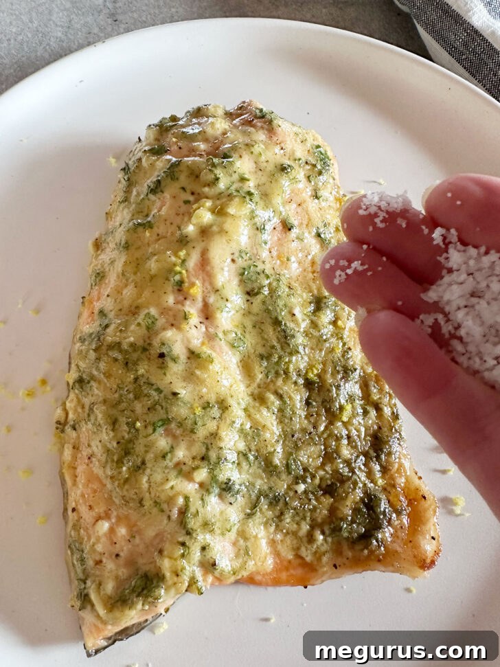 Flaky salt is sprinkled over the golden-brown cooked salmon, adding a final touch of seasoning and texture.