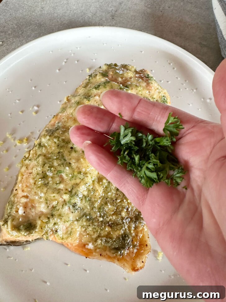 Finely chopped fresh parsley is sprinkled over the cooked salmon, providing a vibrant garnish and fresh aroma.
