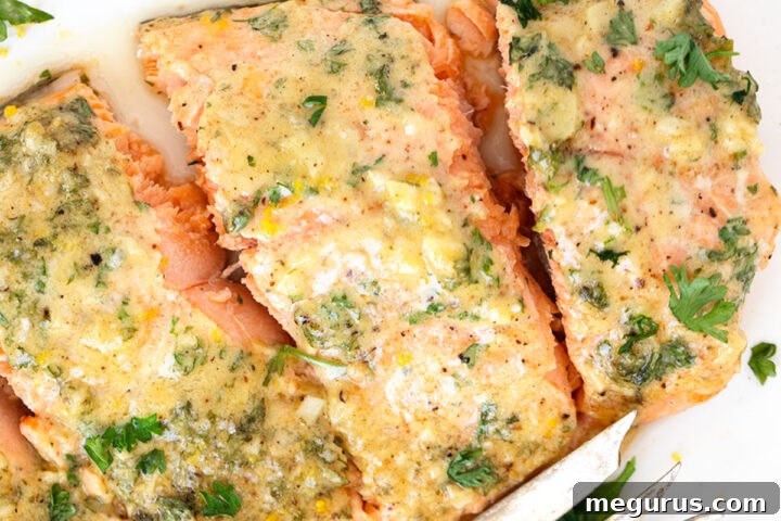 A close-up of the finished Dijon Mustard Garlic Salmon on a white plate, showcasing its golden topping and flaky texture, garnished with fresh herbs.